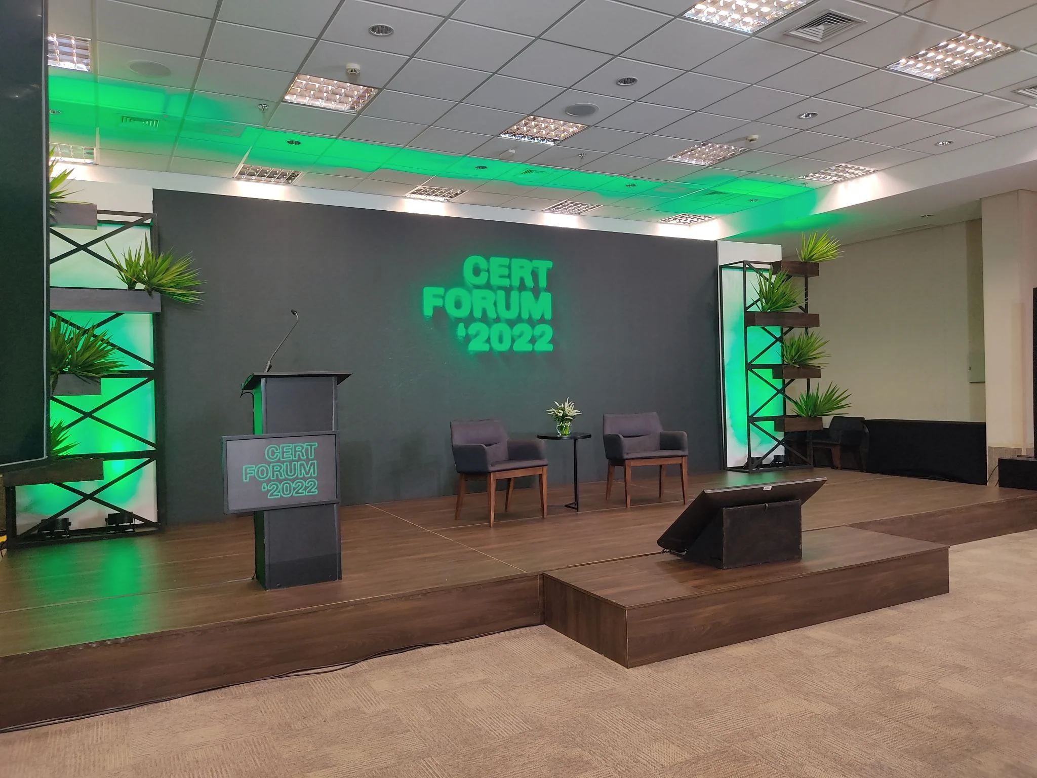 Palco do CERT Fórum 2022 com iluminação verde e painel de fundo